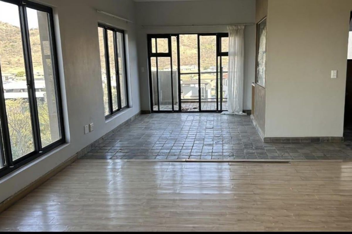 An empty living area featuring a mix of tiled and laminate flooring, large aluminium windows, and sliding glass doors leading to an outdoor space.