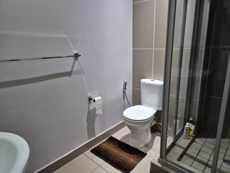 A clean, functional bathroom featuring a modern toilet, a glass-enclosed shower, and neutral wall and floor tiling.