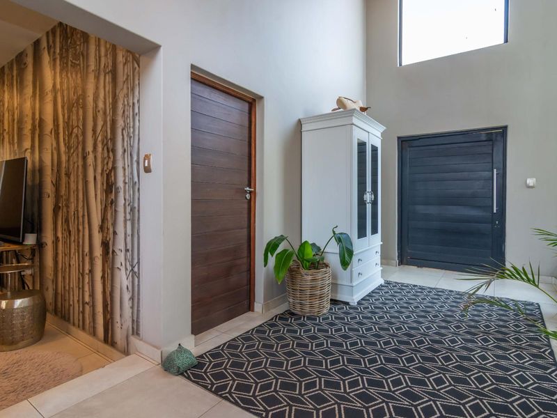 Spacious entrance hall featuring double-height ceilings, a high-level window for natural light, modern tiled flooring, and a solid timber front door.