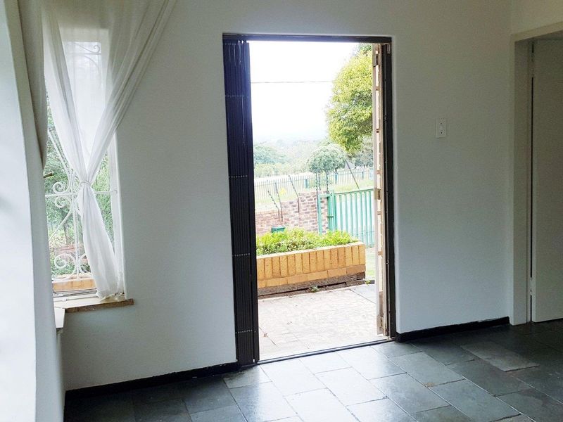 An empty living area featuring slate tile flooring, wrought iron security bars on the windows, and direct access to an outdoor patio area.