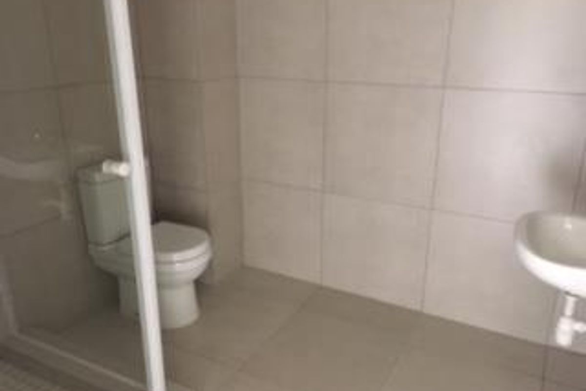 A clean, modern bathroom featuring neutral wall and floor tiling, a glass-enclosed shower, a white toilet, and a wall-mounted basin.