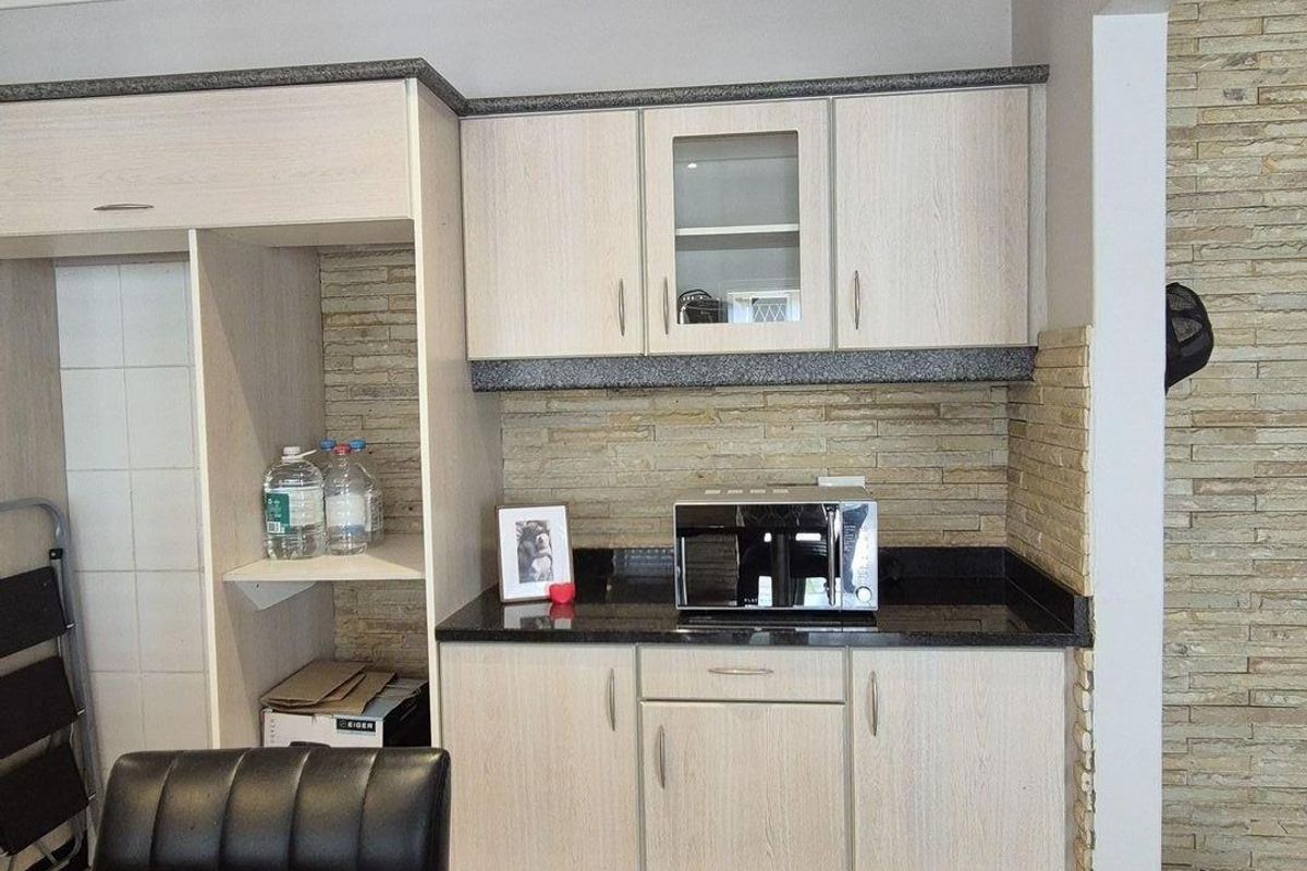 A kitchen area featuring light wood-grain cabinetry, dark granite countertops, and a textured stone-cladding backsplash.