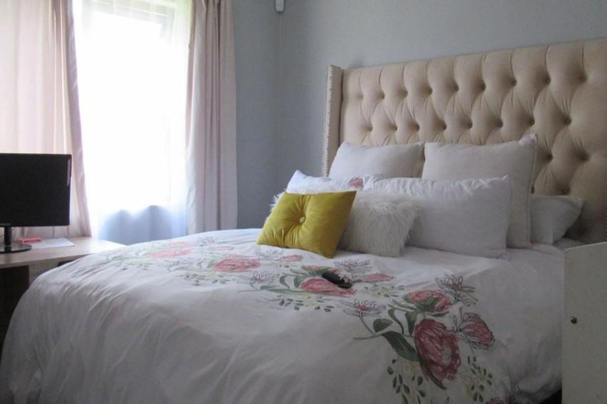 A well-lit bedroom featuring a neutral color palette, large window with curtains, and space for a bed and desk setup.