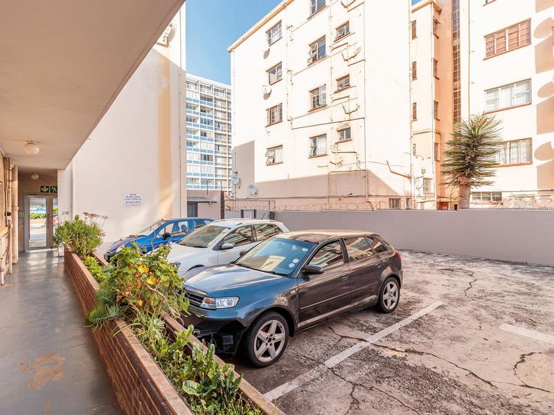 Exterior view of the apartment complex rear parking area featuring a brick planter box and a covered walkway.