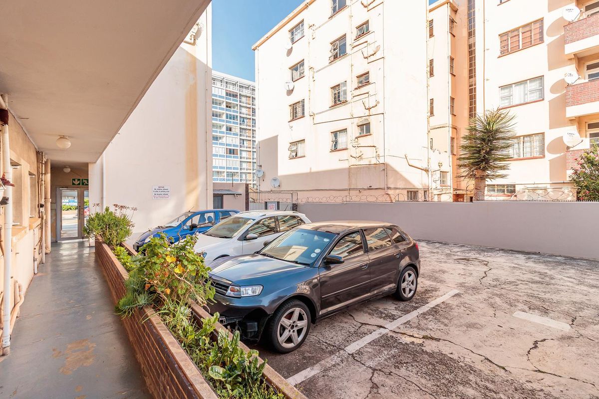 Exterior view of the apartment complex rear parking area featuring a brick planter box and a covered walkway.