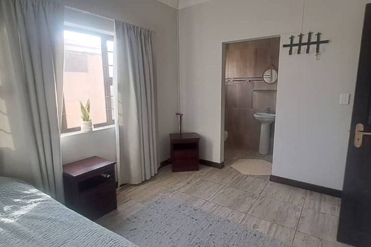 A bedroom featuring tiled flooring, built-in cupboards, and an adjoining en-suite bathroom with a pedestal basin.