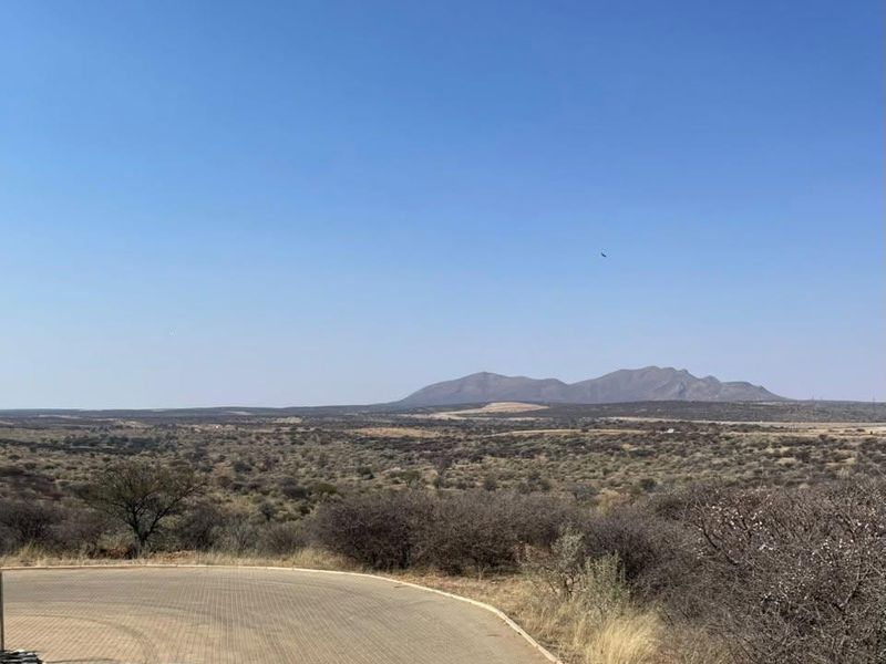 Expansive scenic view overlooking natural bushveld landscape and distant mountains from a paved residential access point.