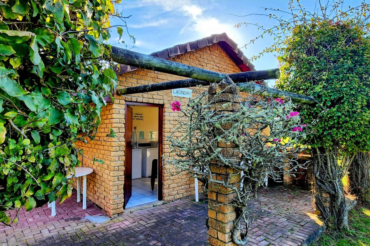 Exterior view of a brick-built laundry facility featuring a timber pergola structure and paved patio area set within a garden.