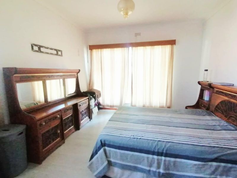 A standard bedroom featuring neutral walls, tiled flooring, and a large window with curtain rails.
