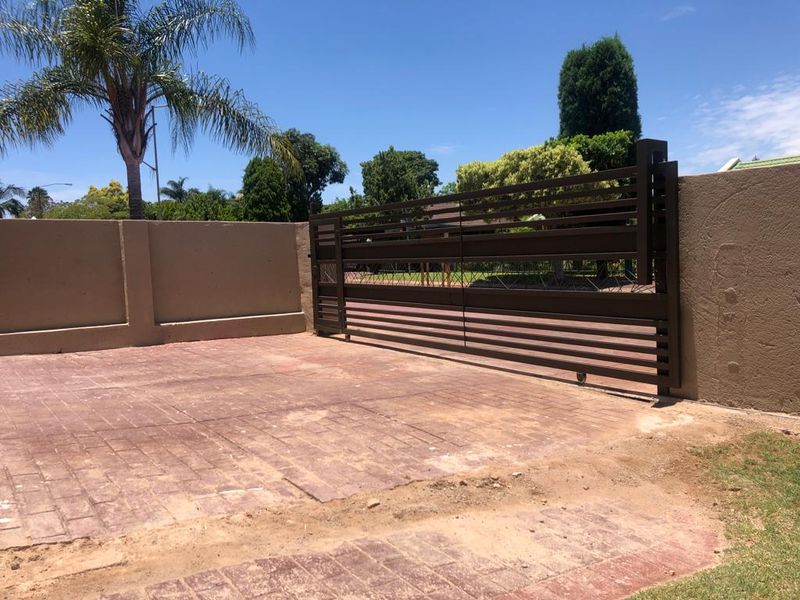 A secure modern horizontal slat driveway gate set within a perimeter boundary wall, featuring a paved entrance area.