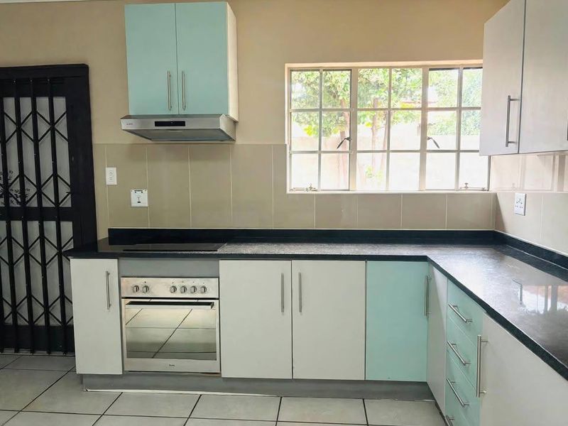 A functional kitchen featuring two-tone cabinetry, built-in oven with hob, extractor fan, tiled splashbacks, and durable tiled flooring.