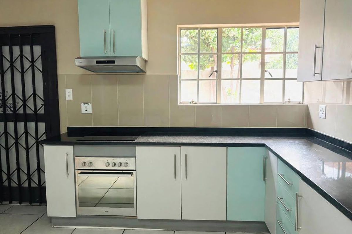 A functional kitchen featuring two-tone cabinetry, built-in oven with hob, extractor fan, tiled splashbacks, and durable tiled flooring.
