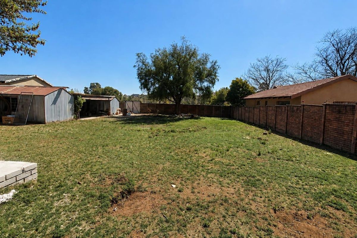 Spacious rear garden featuring a brick boundary wall, a corrugated metal storage shed, and a concrete patio foundation.