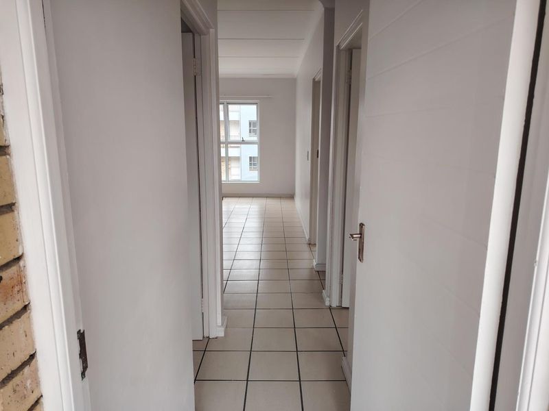 A bright, empty hallway featuring neutral tiled flooring and multiple internal doors leading to various rooms within the apartment.