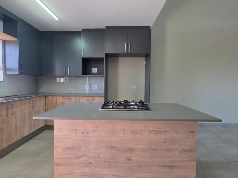 Modern kitchen featuring a central island with a gas hob, ample built-in cabinetry, stone countertops, and neutral tiled flooring in an open-plan layout.