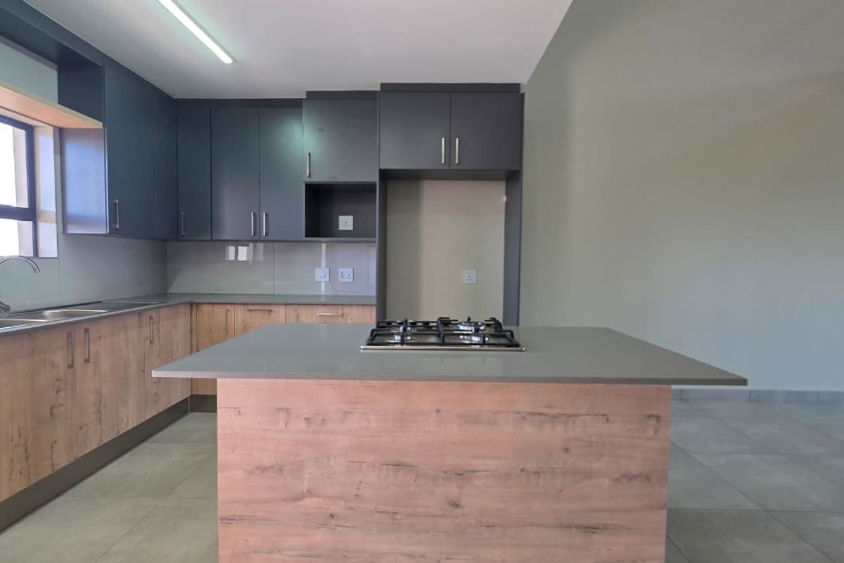 Modern kitchen featuring a central island with a gas hob, ample built-in cabinetry, stone countertops, and neutral tiled flooring in an open-plan layout.
