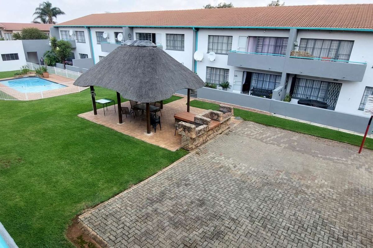 Elevated view of a communal townhouse complex featuring a landscaped garden, swimming pool, and a thatched lapa with a built-in braai area.
