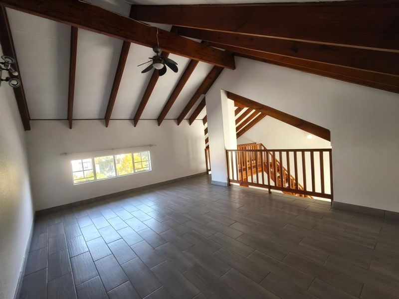 Spacious open-plan living area featuring high vaulted ceilings with exposed timber beams, modern tiled flooring, and a timber staircase balustrade.