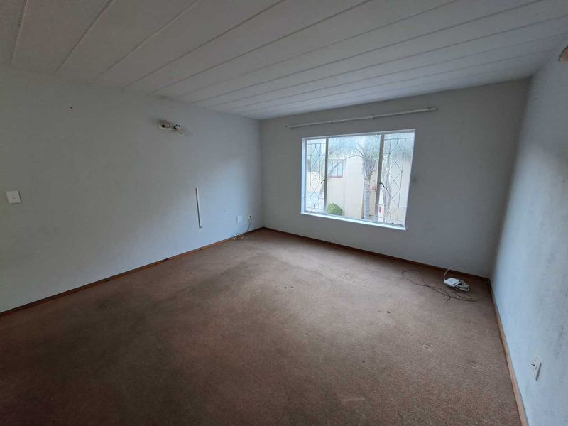 An empty bedroom featuring carpeted flooring, exposed beam ceilings, and a window with security bars, requiring cosmetic updates.