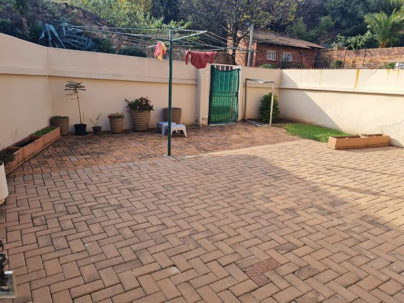 A paved rear courtyard area enclosed by a perimeter wall with a security gate, providing a private outdoor space.