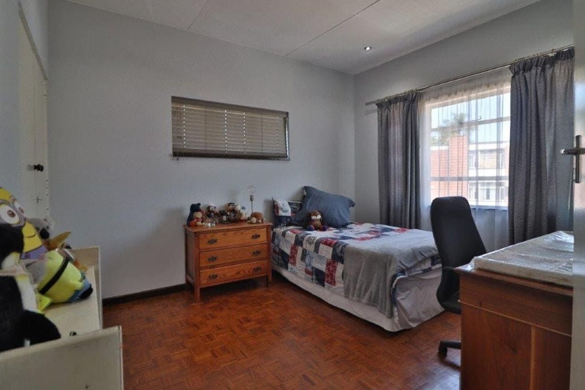 A bedroom featuring parquet flooring, built-in cupboards, and a window with security bars, offering a functional space with natural light.