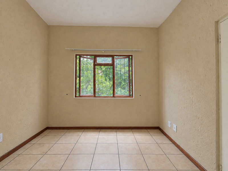 An empty bedroom featuring tiled flooring, textured walls, and a timber-framed window with security bars, offering a blank canvas for personalization.