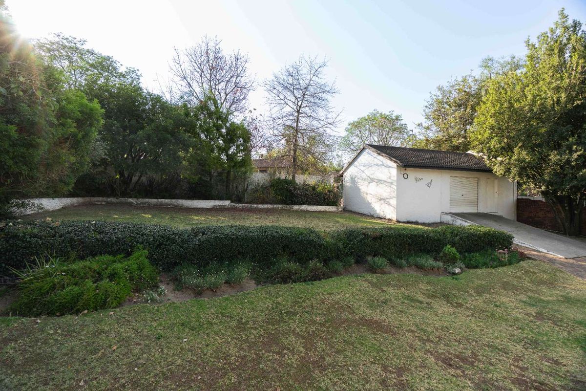 A spacious rear garden featuring a detached garage, concrete driveway, and established landscaping with a retaining wall.