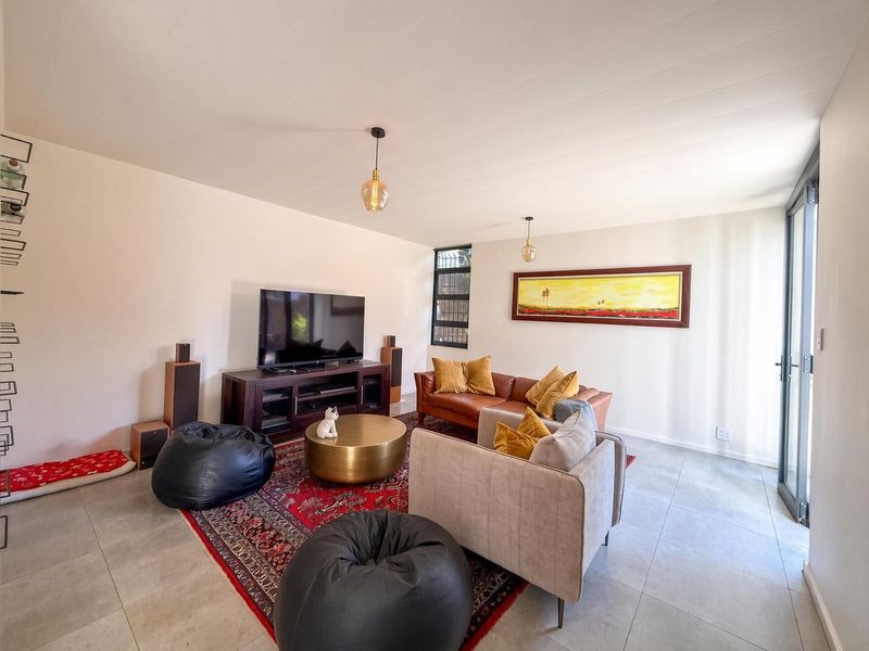 A bright and spacious living room featuring neutral tiled flooring, modern pendant lighting, and a large sliding glass door providing access to the exterior.