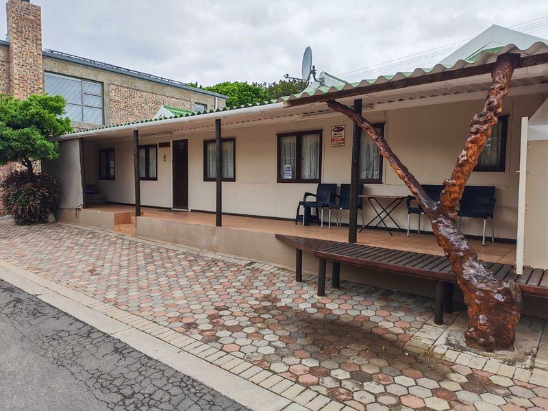 A single-story exterior view featuring a covered patio area with tiled flooring, timber supports, and a paved driveway approach.