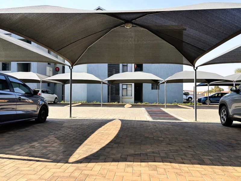 Covered parking area with shade cloth structures and paved driveway located in front of the apartment building.