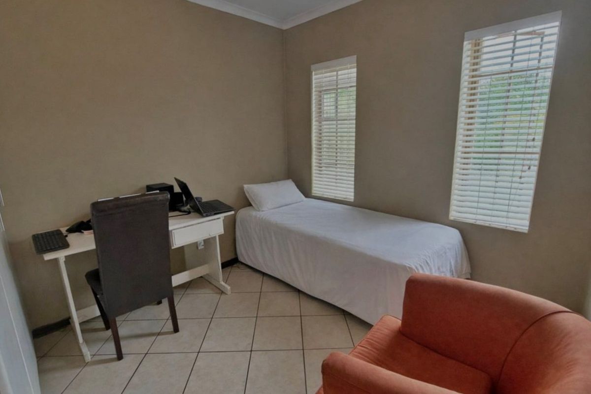 A functional bedroom featuring neutral wall tones, tiled flooring, and dual windows fitted with horizontal blinds.