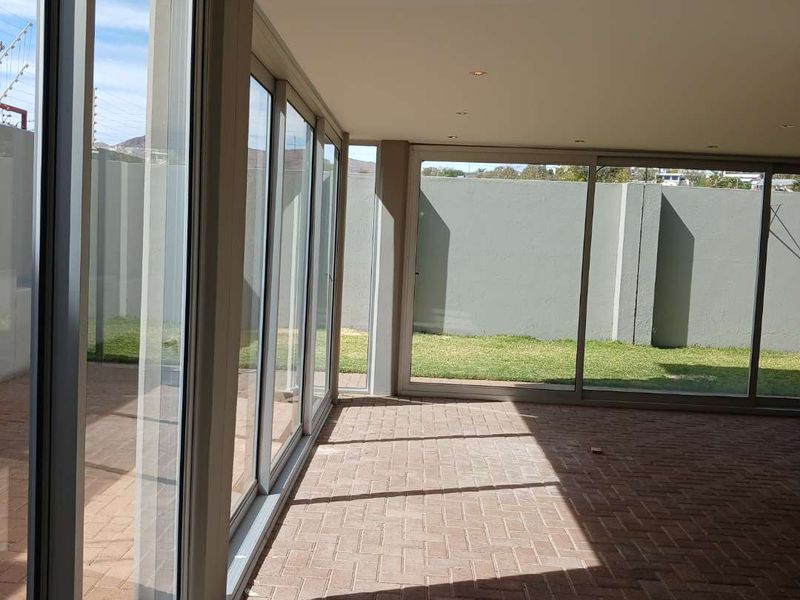A spacious, covered patio area featuring brick paver flooring and large sliding glass doors that open onto a private garden space.