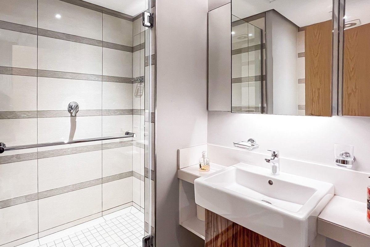 Modern bathroom featuring a glass-enclosed shower with tiled walls, a sleek vanity basin with storage, and a mirrored cabinet.
