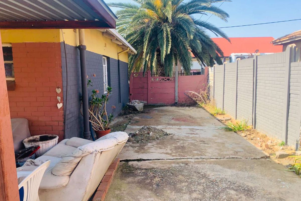 Rear exterior area featuring concrete paving, a precast boundary wall, and a metal gate, with a covered patio section.