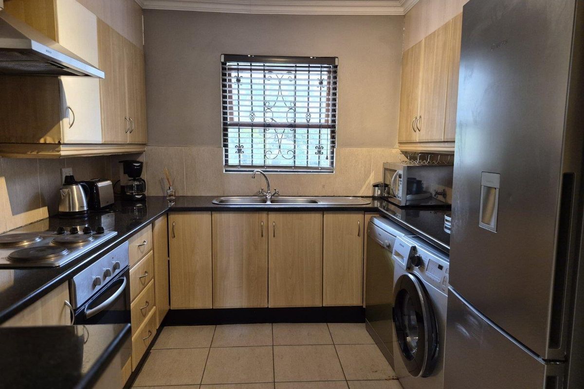 A functional galley-style kitchen featuring light wood-finish cabinetry, dark granite countertops, a double sink, and integrated space for laundry appliances.