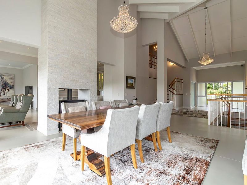 Spacious open-plan living and dining area featuring a striking stone-clad fireplace, vaulted ceilings, and elegant chandeliers, creating a bright and airy atmosphere.