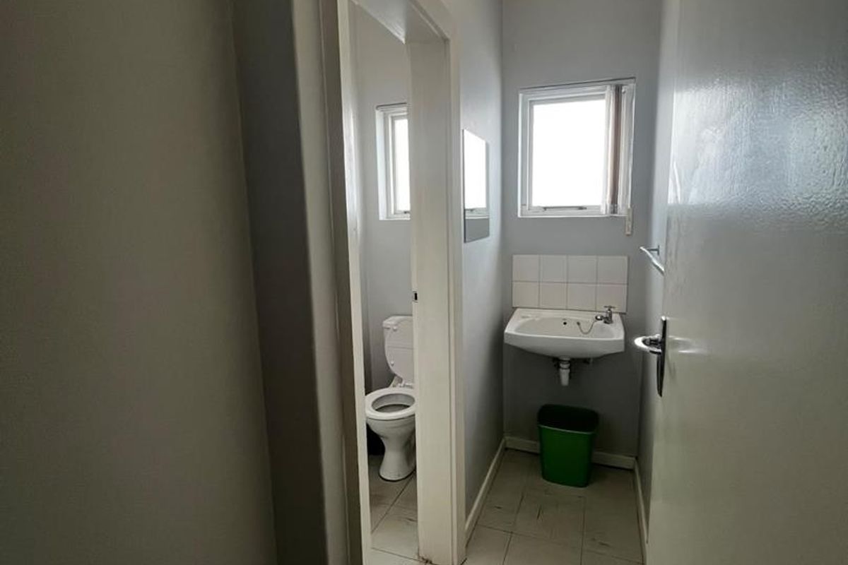 A compact, functional bathroom featuring a wall-mounted basin and toilet with neutral wall finishes and tiled flooring.