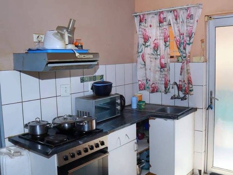 Compact kitchen featuring a built-in oven, hob, extractor fan, and tiled splashback, with direct access to an exterior door.
