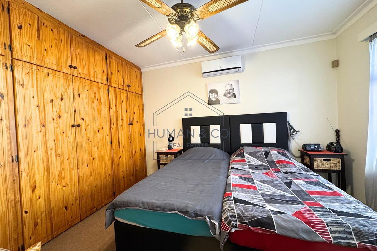A bedroom featuring built-in wooden cabinetry, a ceiling fan, and a wall-mounted air conditioning unit.