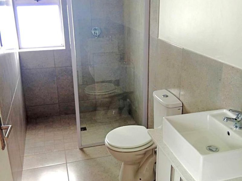 A clean, modern bathroom featuring a glass-enclosed shower, a white vanity with a vessel sink, and neutral floor-to-ceiling tiling.
