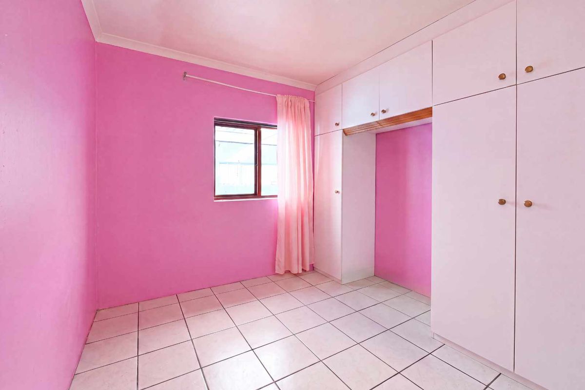 A bright, empty bedroom featuring tiled flooring and extensive built-in cupboard storage, ready for personalization.