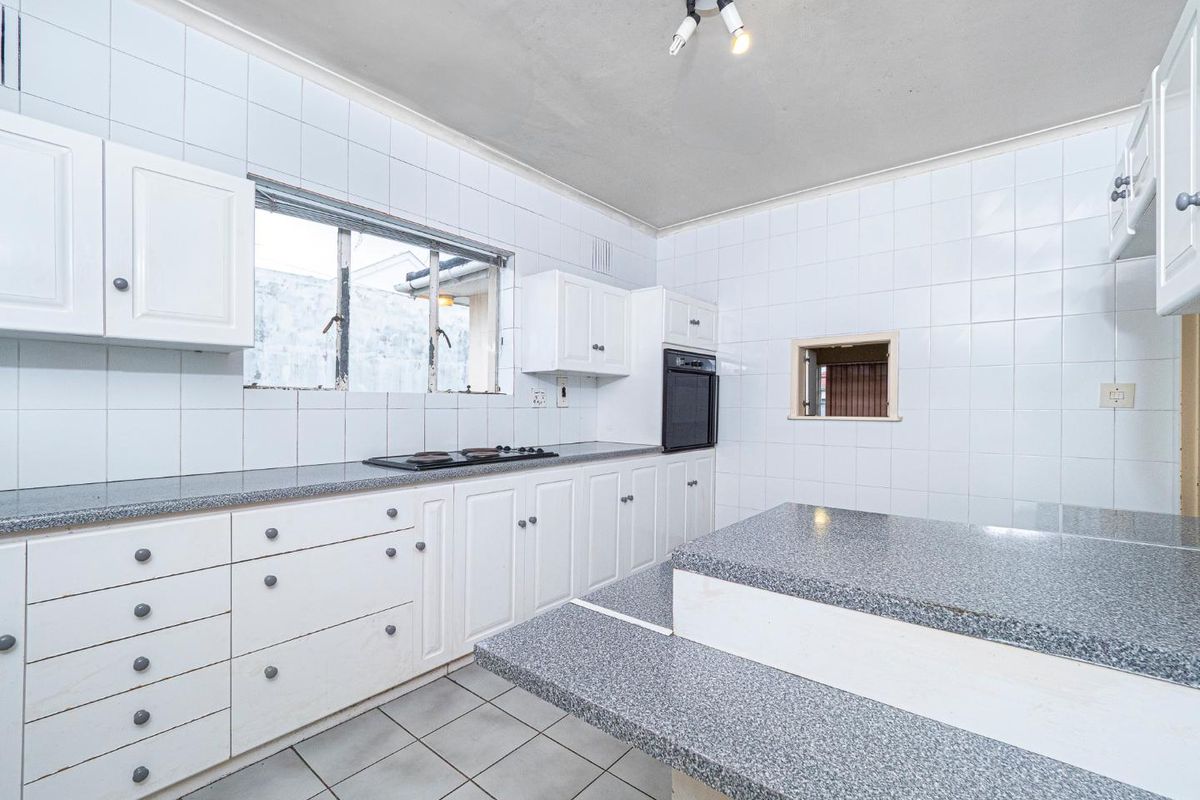 A functional kitchen featuring white cabinetry, granite-look countertops, a built-in oven, and a central island, finished with full-height wall tiling.