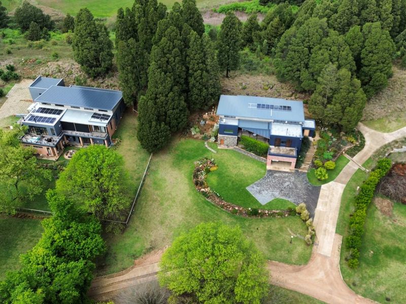 Aerial view of a residential property featuring two modern homes with solar panels, expansive landscaped gardens, and paved driveway access.