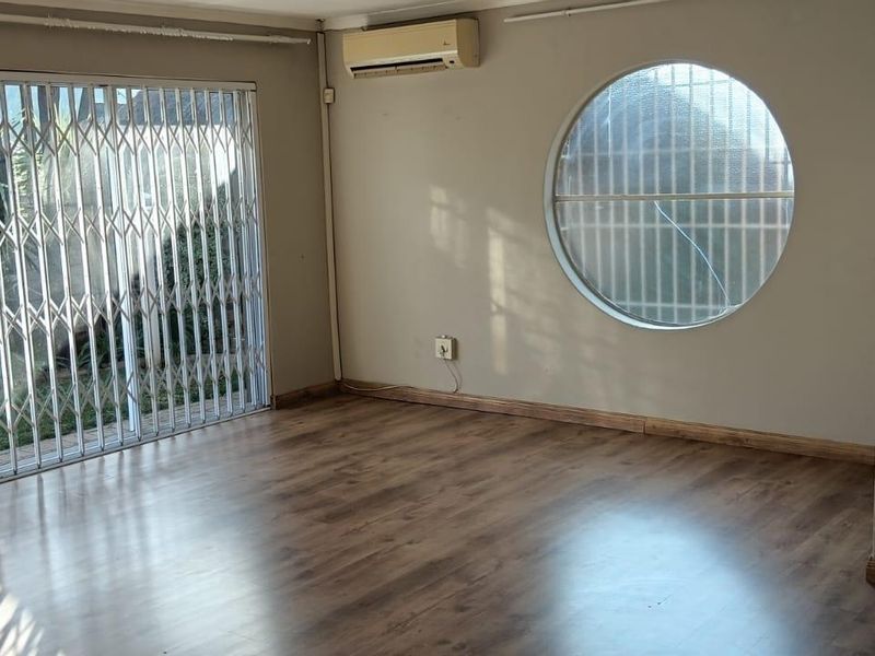 An empty living room featuring laminate flooring, a split-system air conditioner, and a distinctive circular window with a security gate on the sliding door.