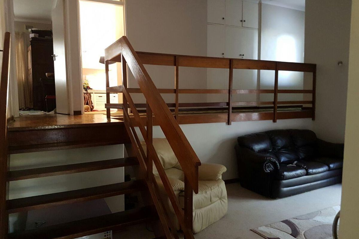 Living area featuring a wooden staircase with balustrade and built-in storage cupboards, providing access to an elevated mezzanine level.