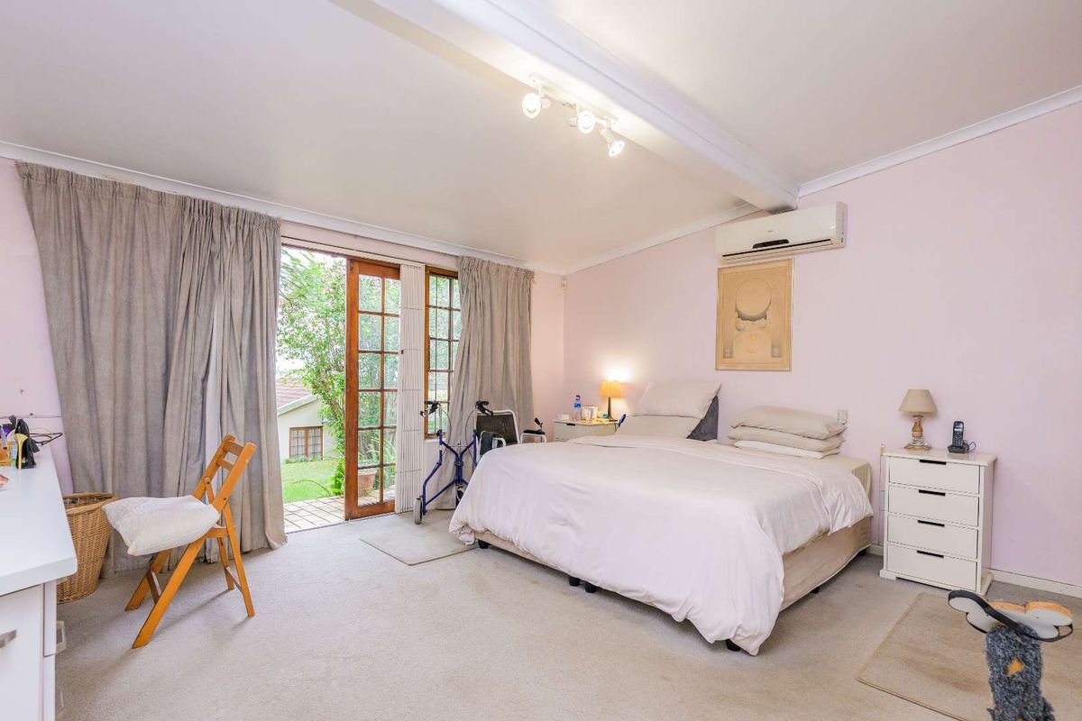 Spacious bedroom featuring neutral carpeting, a wall-mounted air conditioning unit, and direct access to the garden through wooden-framed glass doors.