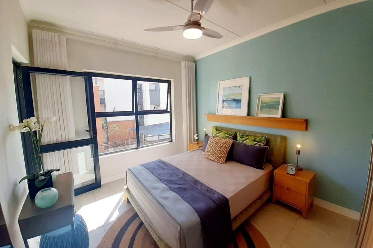 A well-lit bedroom featuring a ceiling fan, tiled flooring, and a large window providing natural light and access to an outdoor area.