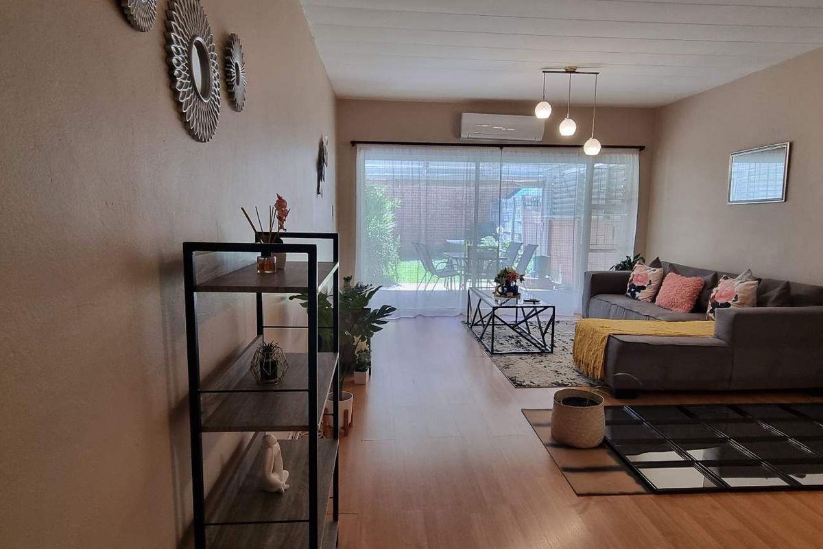 A spacious living room featuring wood-look flooring, a wall-mounted air conditioning unit, and large sliding glass doors providing access to the rear patio.