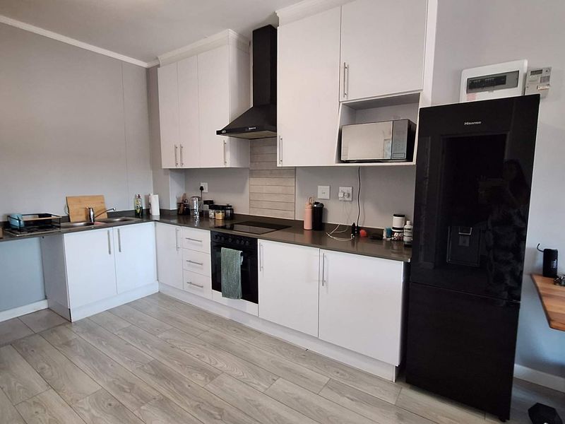 Modern kitchen featuring white cabinetry, dark countertops, integrated oven and hob, extractor fan, and light wood-look laminate flooring.