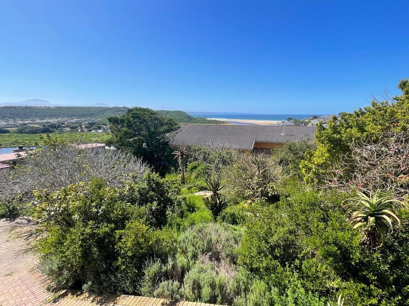 A scenic elevated view overlooking lush coastal vegetation, surrounding landscape, and distant ocean horizon under a clear blue sky.